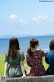 Three women sitting on a wall looking out at the ocean.