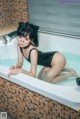 A woman in a black bathing suit sitting in a bathtub.