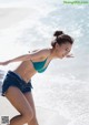 A woman in a blue bikini and denim shorts on the beach.