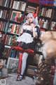 A woman in a maid outfit standing in front of a bookshelf.