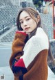 A woman in a brown and white sweater leaning against a wall.